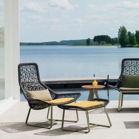 loungestoel met voetenbankje en gele kussens zijaanzicht op een tegelterras met zeezicht