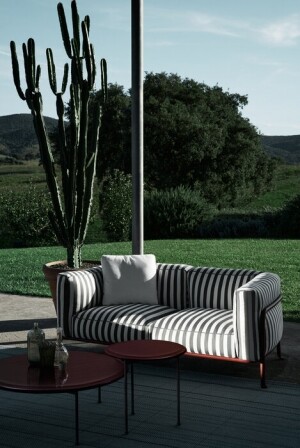 outdoor sofa gestreept met bordeaux tafels voor een groot raam met groen landschap