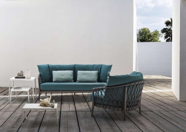 blauwe loungeset met loungestoel en witte tafeltjes voorzijde op een houten platform voor een witte muur