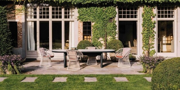 tuintafel met stoelen voorzijde langs een groot huis met begroeiing
